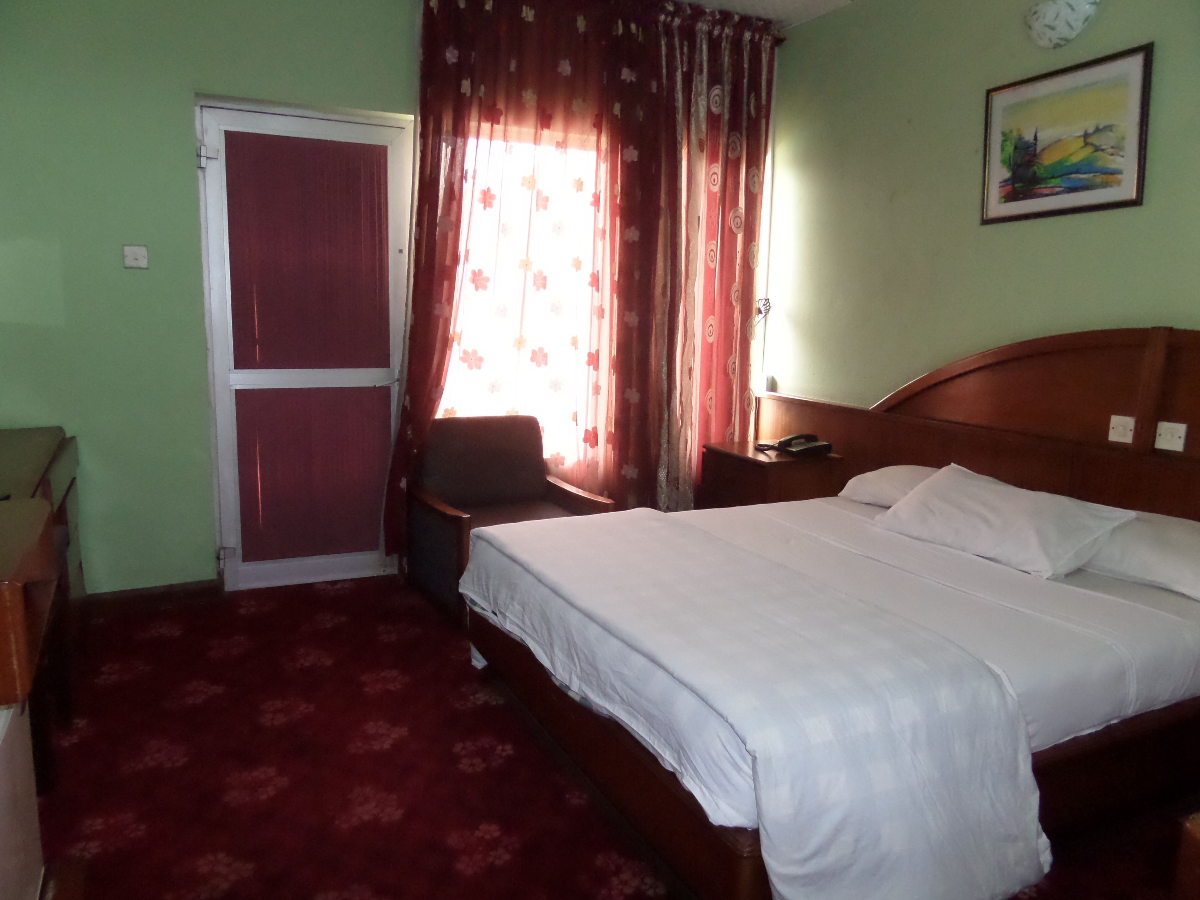 A hotel room with a bed, a chair, a desk, and a door.