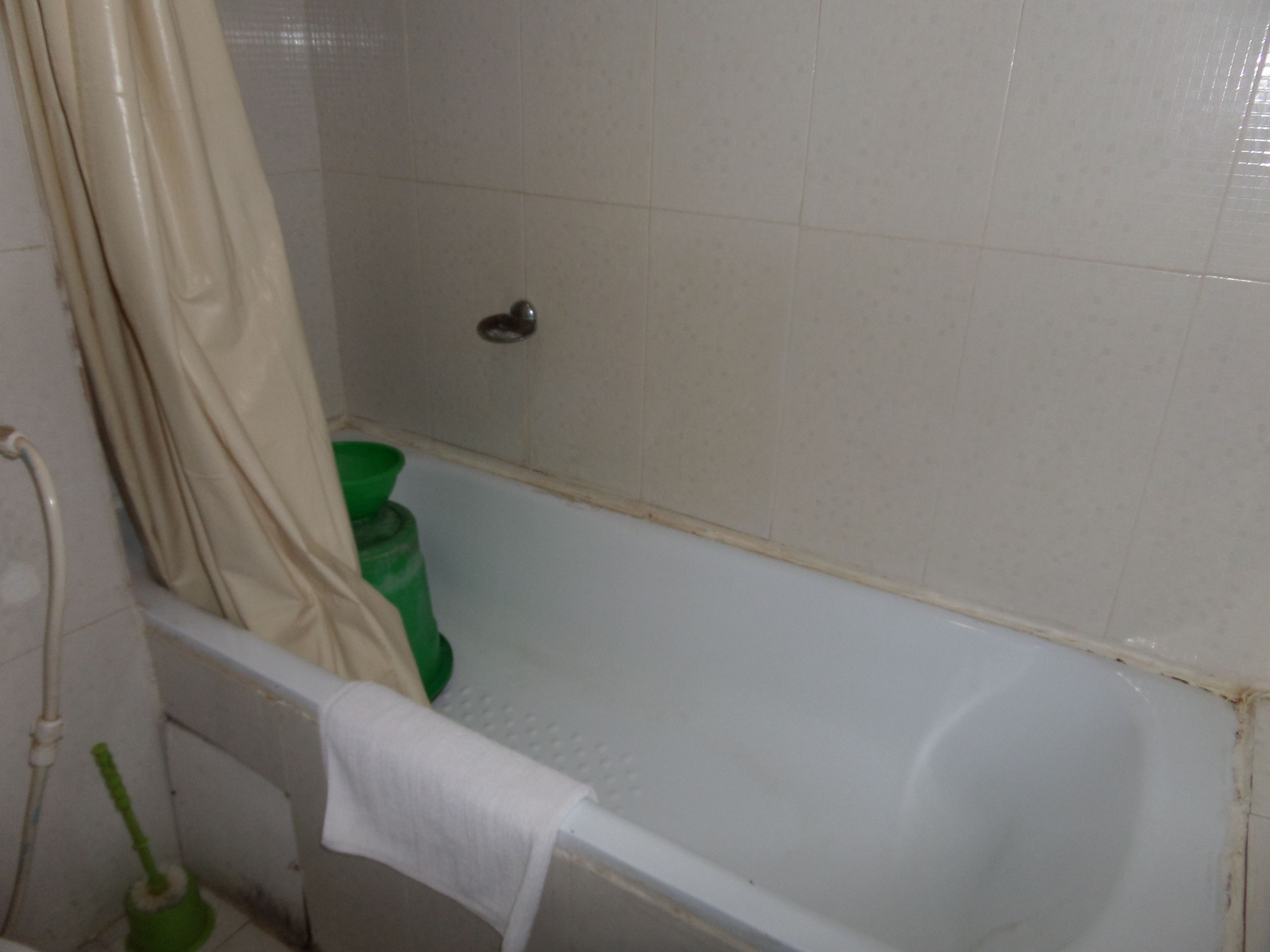 A bathroom with a bathtub, a green bucket, and a white towel.