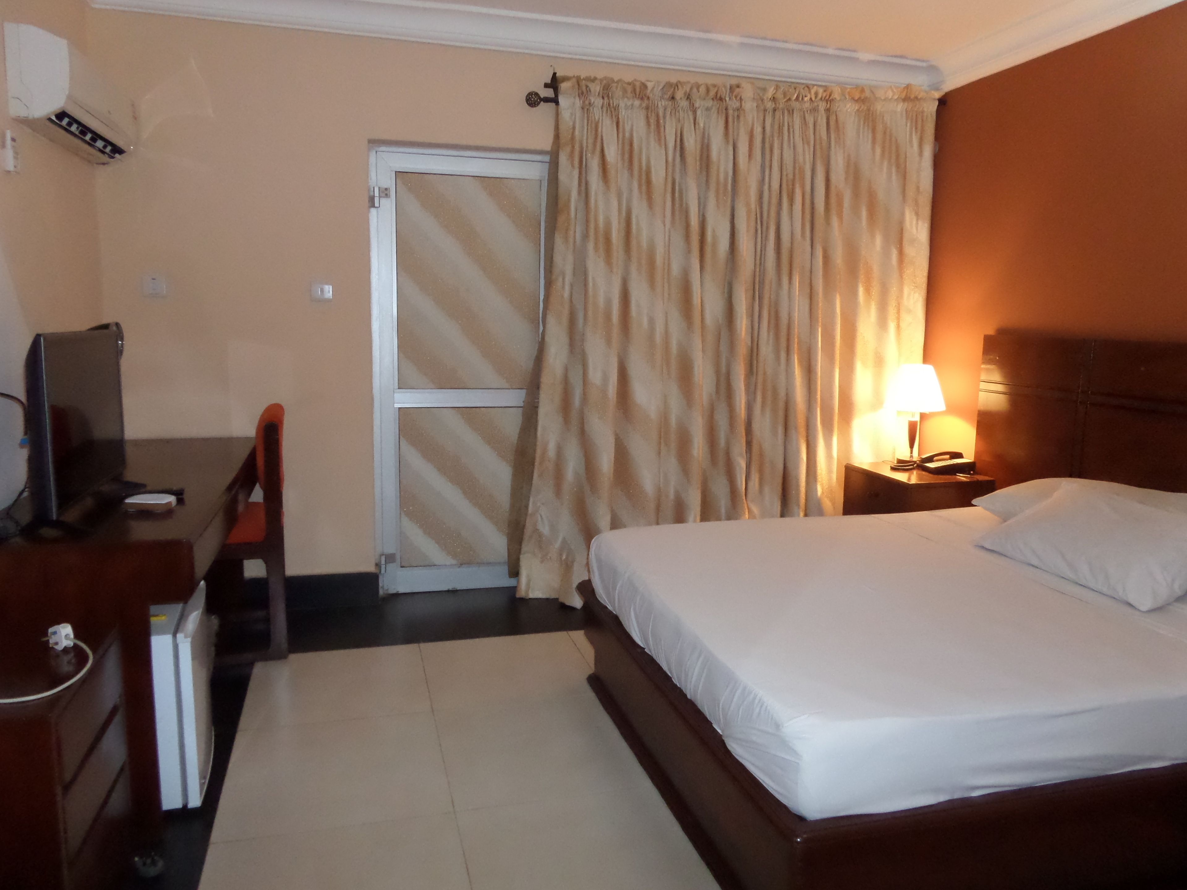 A hotel room with a bed, a desk with a computer, a chair, a lamp, and a telephone on a bedside table.
