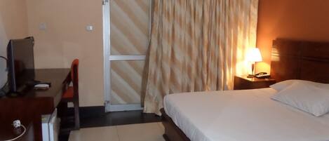 A hotel room with a bed, a desk with a computer, a chair, a lamp, and a telephone on a bedside table.