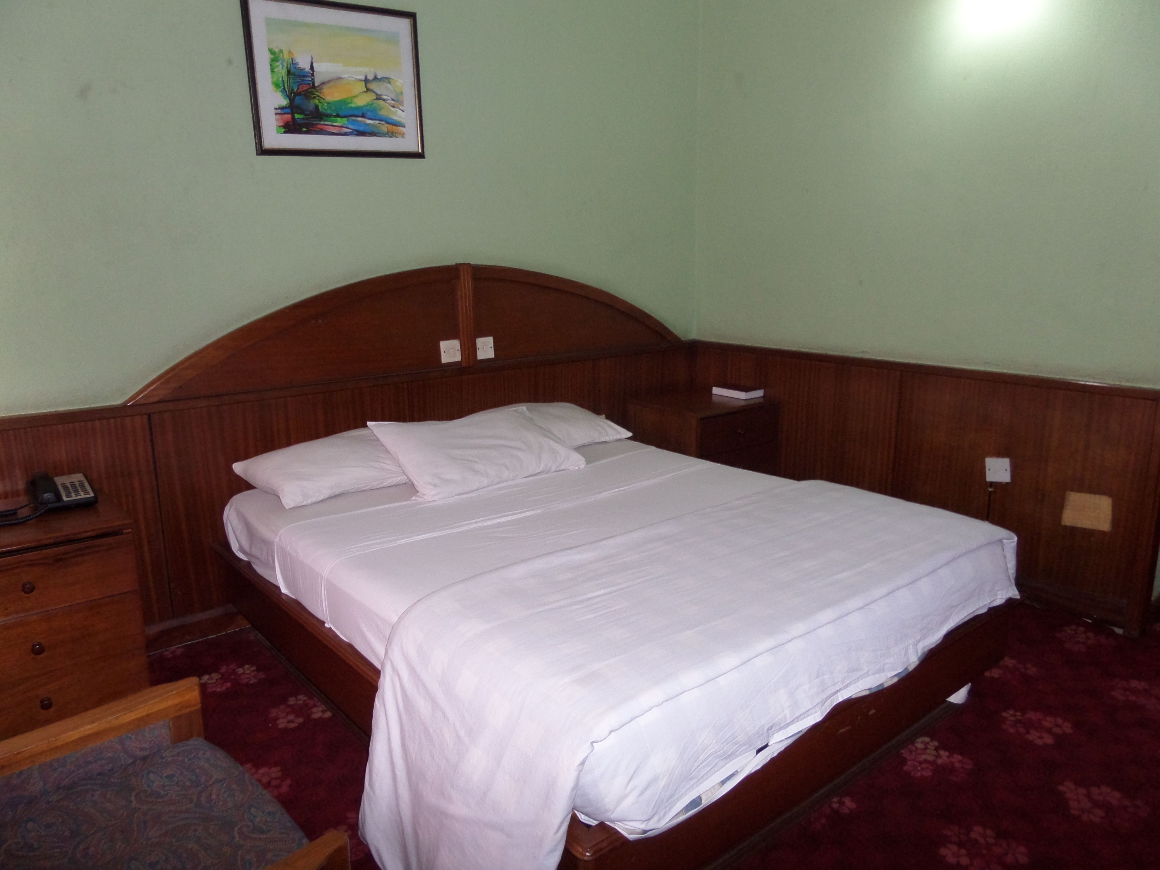 A neatly made bed with white linens in a room with a wooden headboard.