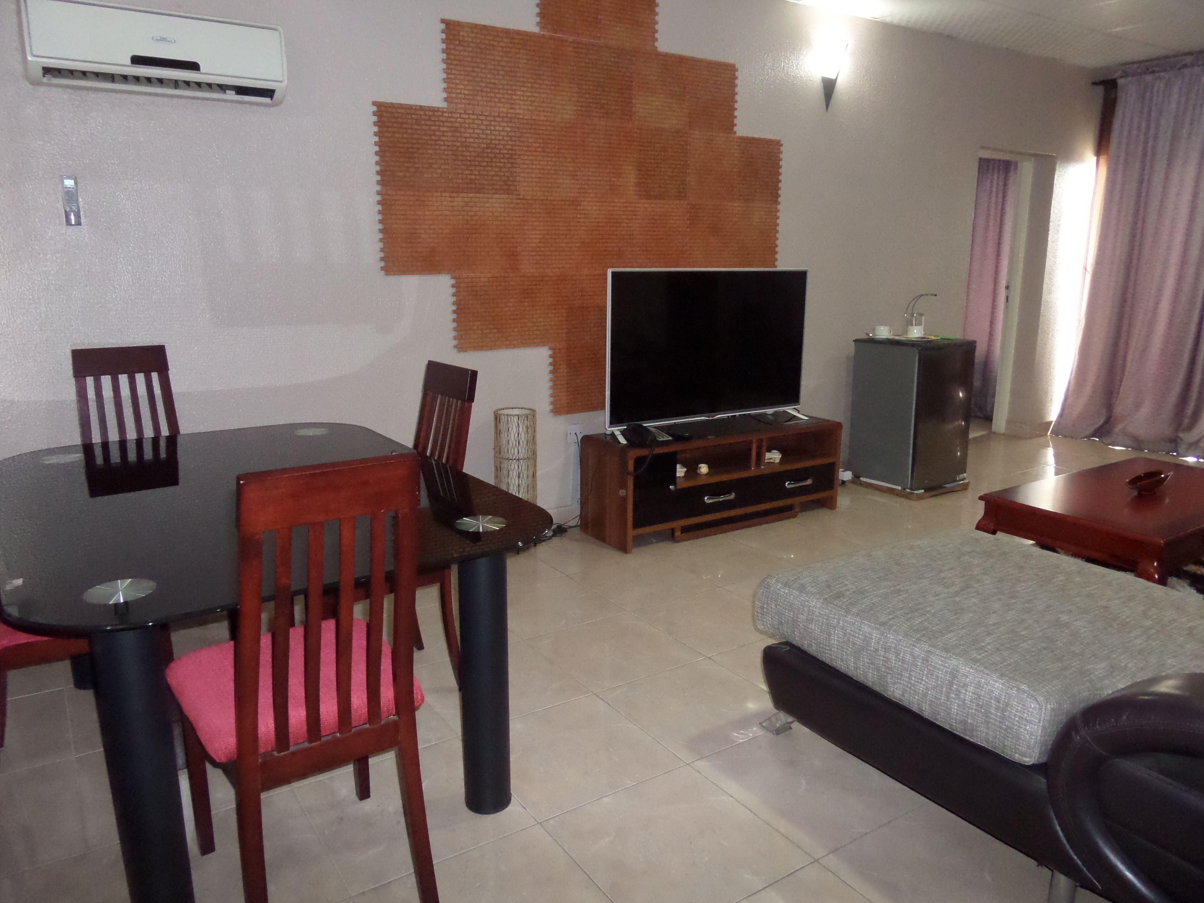 Una sala de estar con televisor, una mesa de comedor, sillas, un sofá y un mueble bajo.