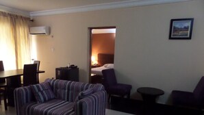 Una sala de estar con un sofá a rayas, una mesa de comedor con sillas, una mesita redonda pequeña y una cama al fondo.