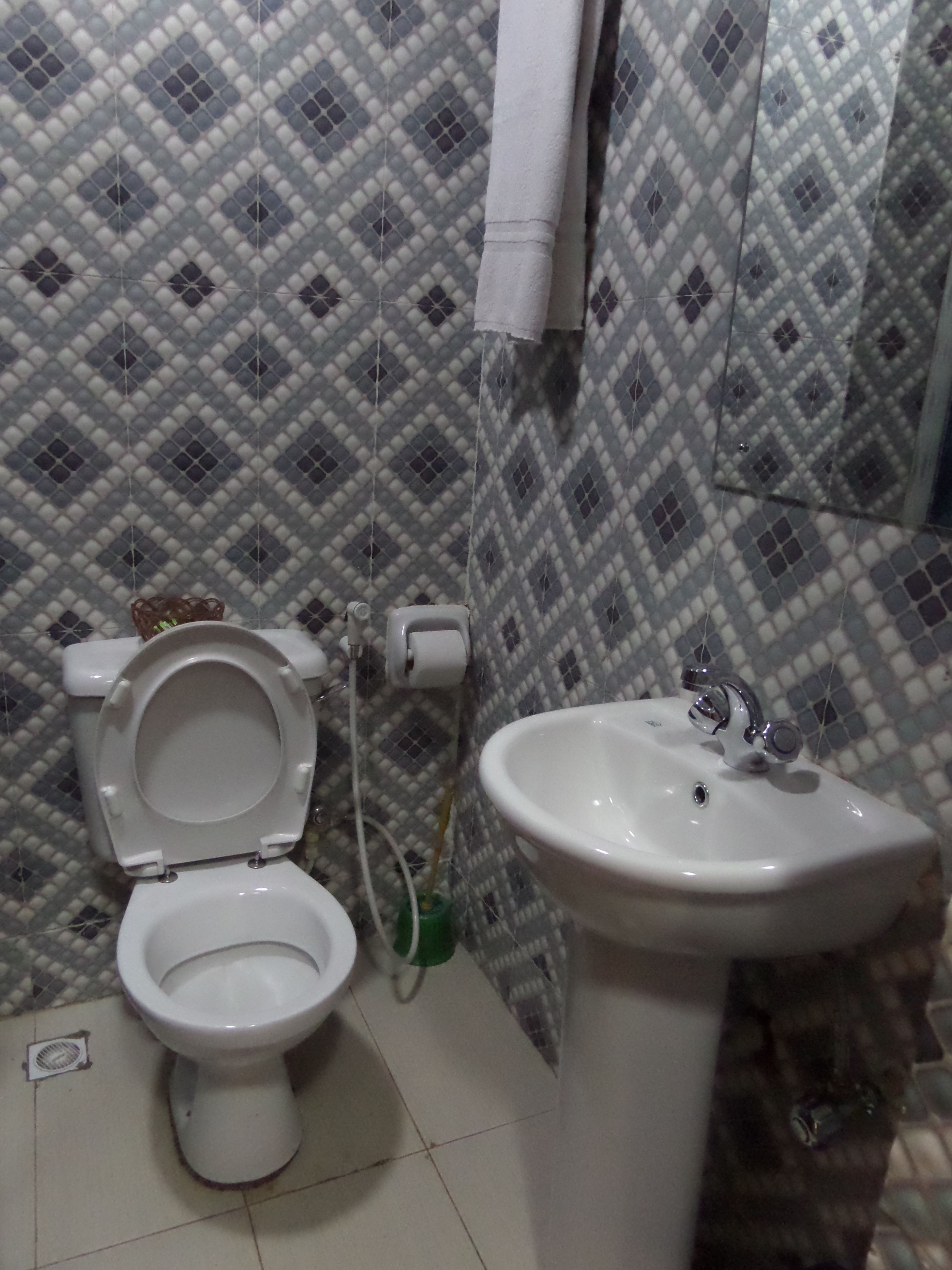 A bathroom with a toilet and a sink, tiled walls, and a hanging towel.