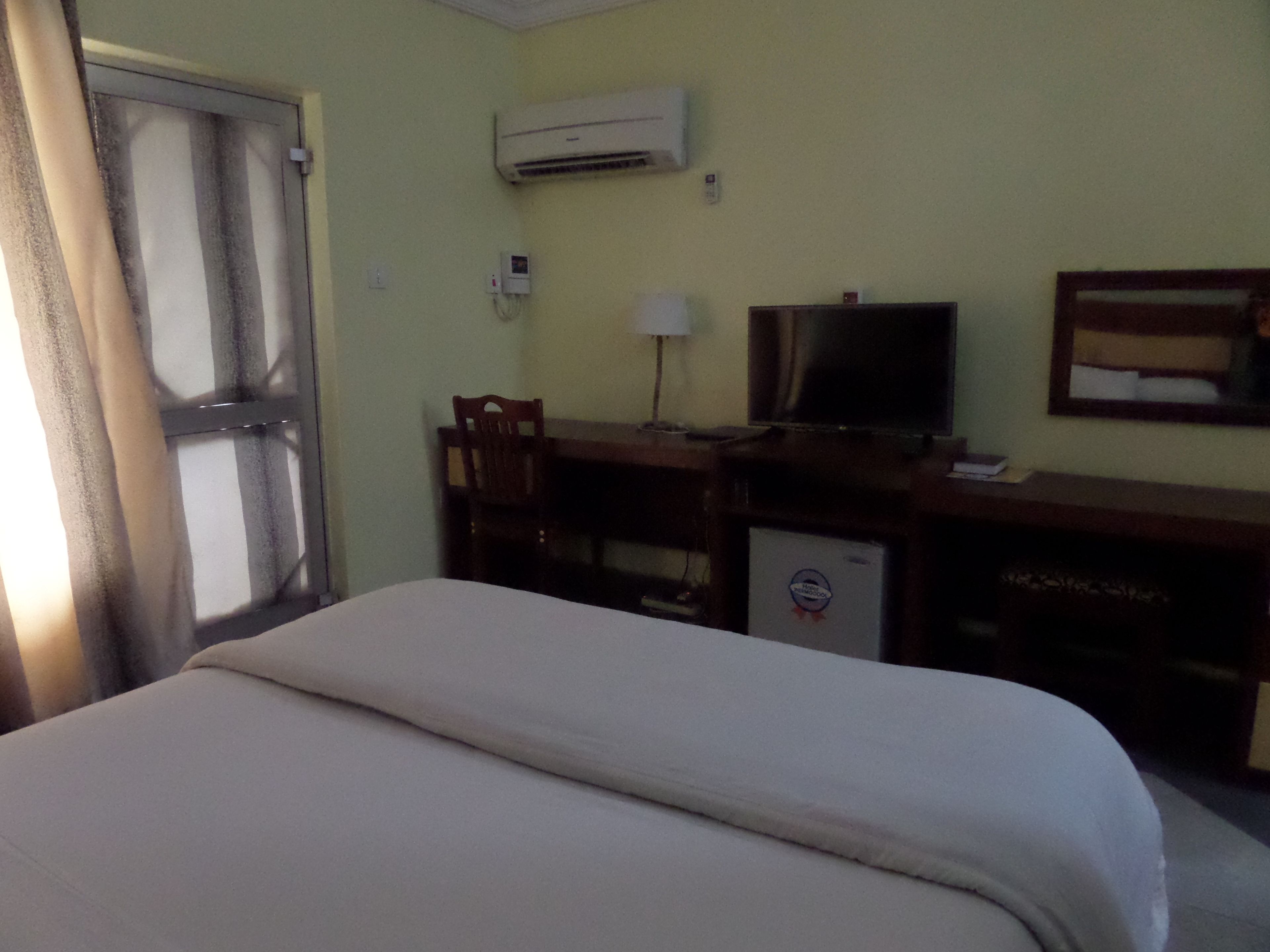 A hotel room with a bed, a desk with a television, and an air conditioning unit on the wall.
