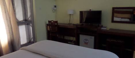 A hotel room with a bed, a desk with a television, and an air conditioning unit on the wall.
