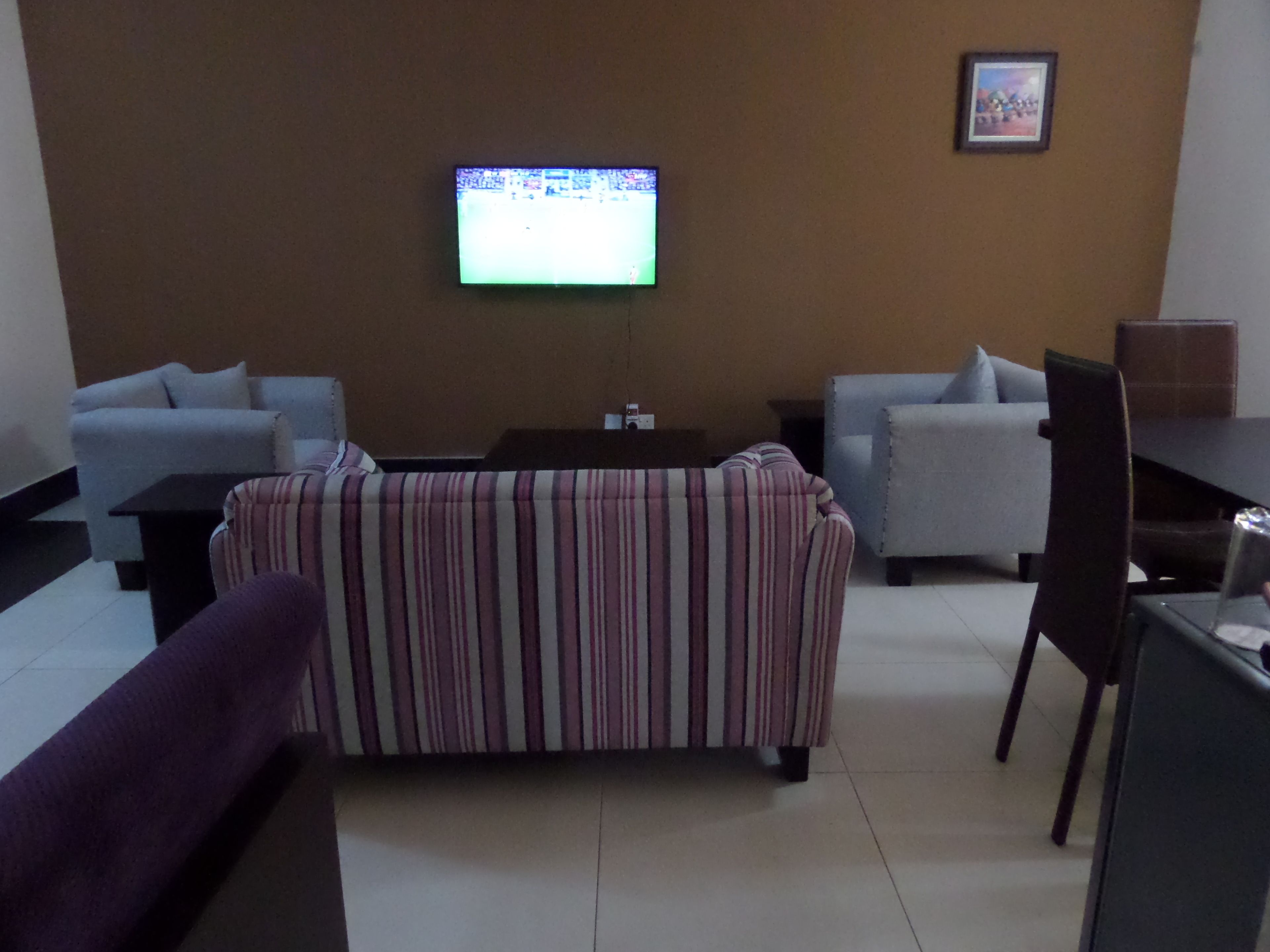 Un salon avec un canapé à rayures, deux fauteuils, une table basse et un téléviseur fixé au mur.