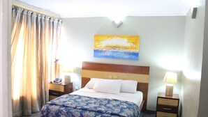 Habitación de hotel con cama, mesitas de noche, un cuadro en la pared y cortinas.