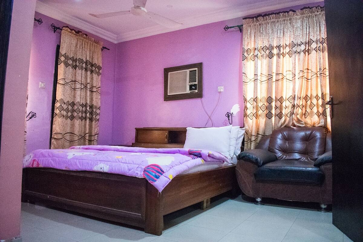 A bedroom with a bed, a chair, and a wall-mounted air conditioner.