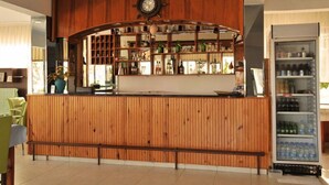 Een bar met houten lambrisering, een klok, planken met flessen en een koelkast.