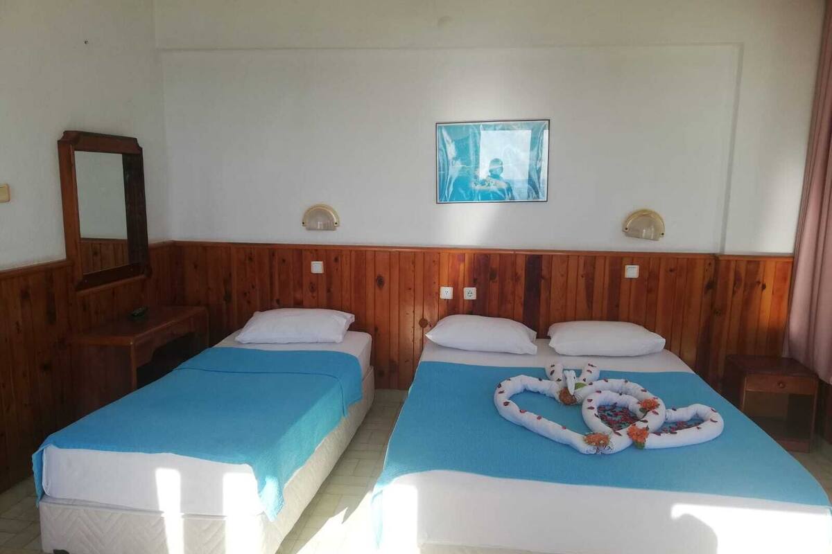 Ein Hotelzimmer mit zwei Einzelbetten, Holzwandverkleidung, einem großen Spiegel und einem gerahmten Bild an der Wand.