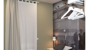 A hotel room with two beds, a large window with curtains, a wall-mounted light, and a wardrobe with hanging clothes. - B&B Stazione Dittaino (Assoro)