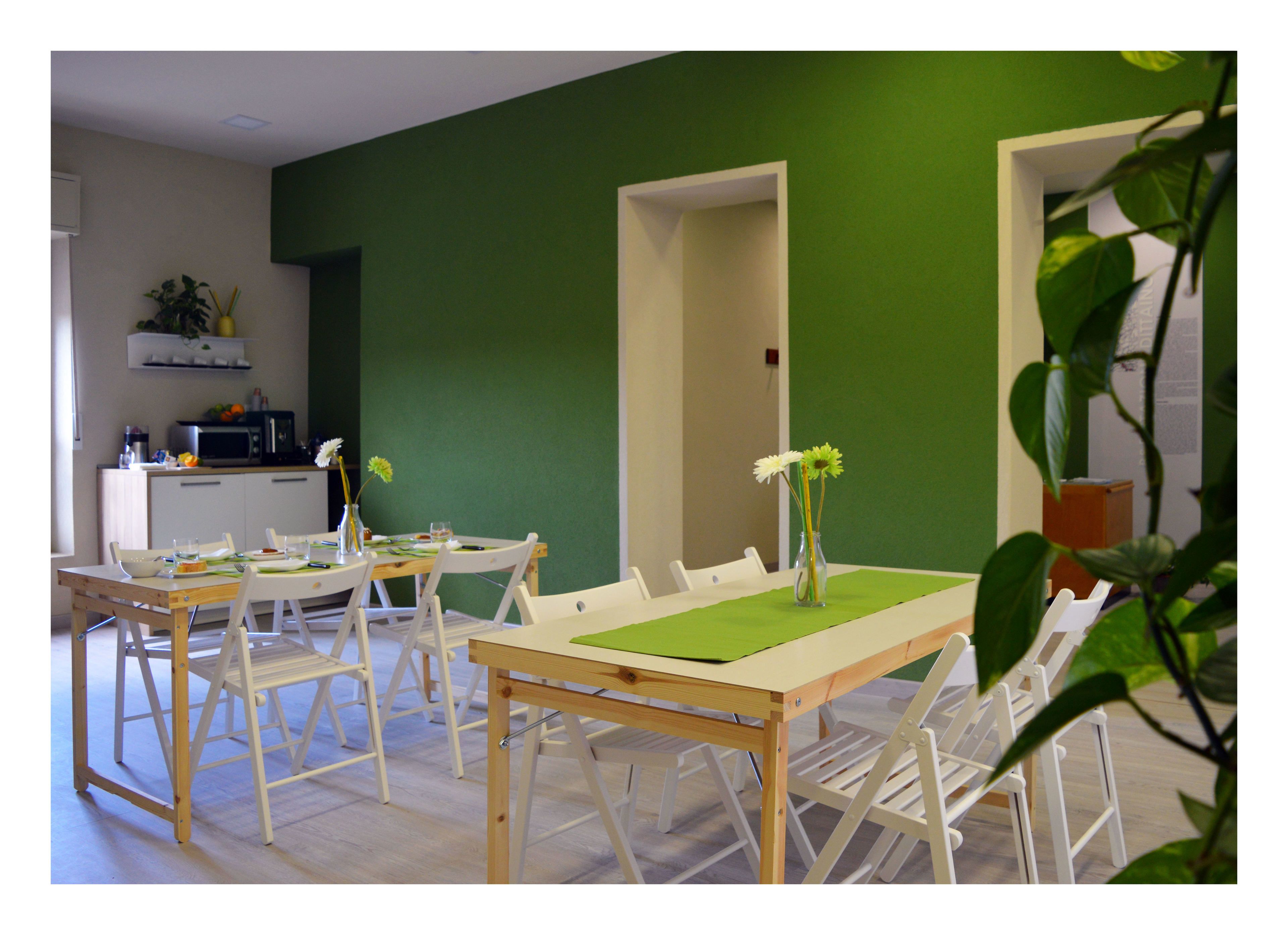Comedor con pared verde, sillas blancas y una mesa dispuesta para cuatro.