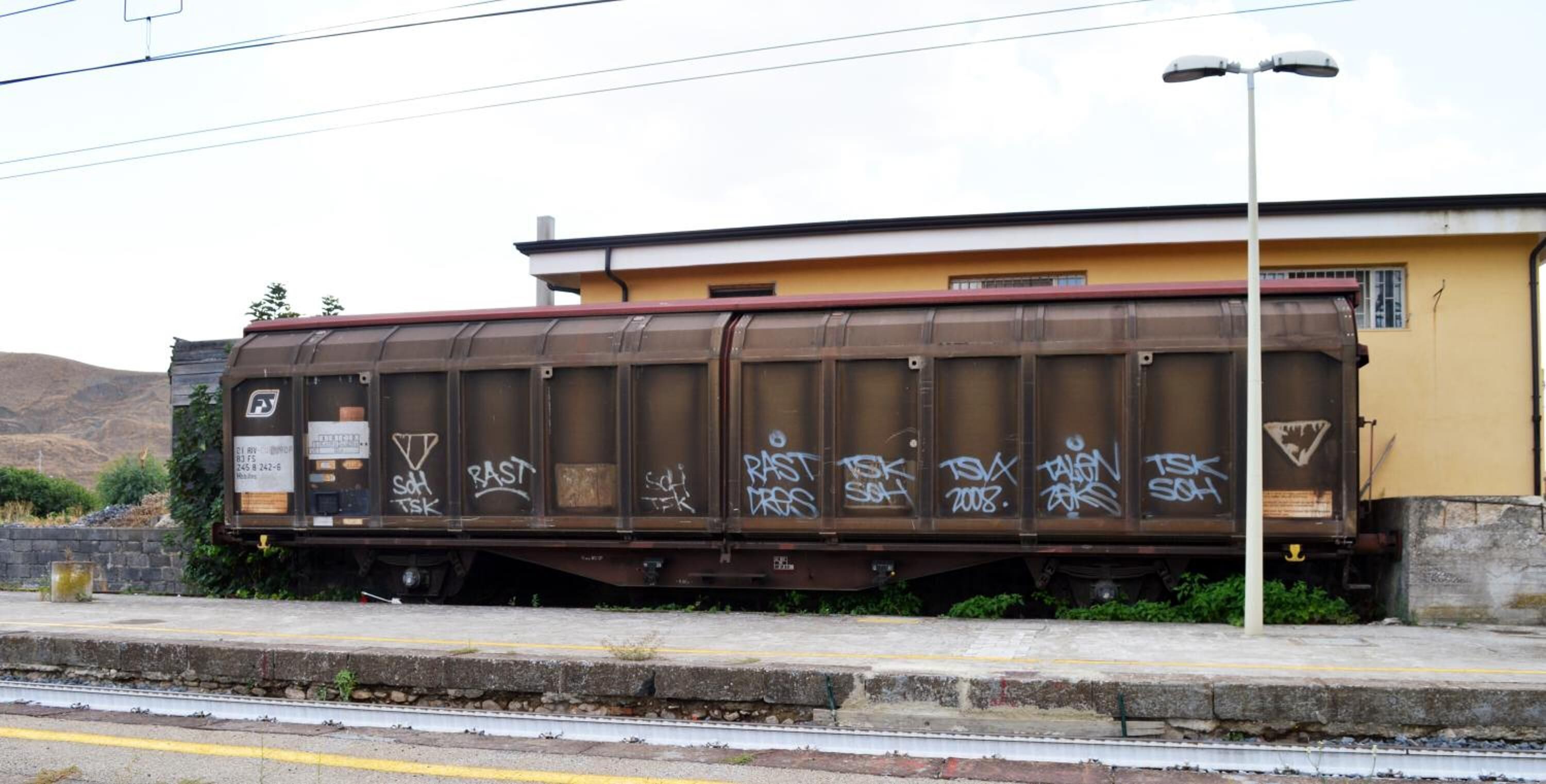 A train car with graffiti, parked next to a building with a yellow facade.