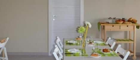 A dining area with a table set for four, chairs, a wooden side table with food, and a door with a window.