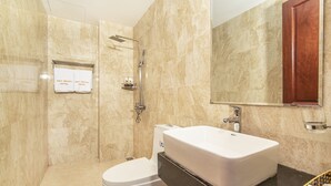 A bathroom with a white sink, a toilet, and a shower. There is a mirror above the sink and a wooden cabinet below it. - May Beach Hotel (Da Nang)