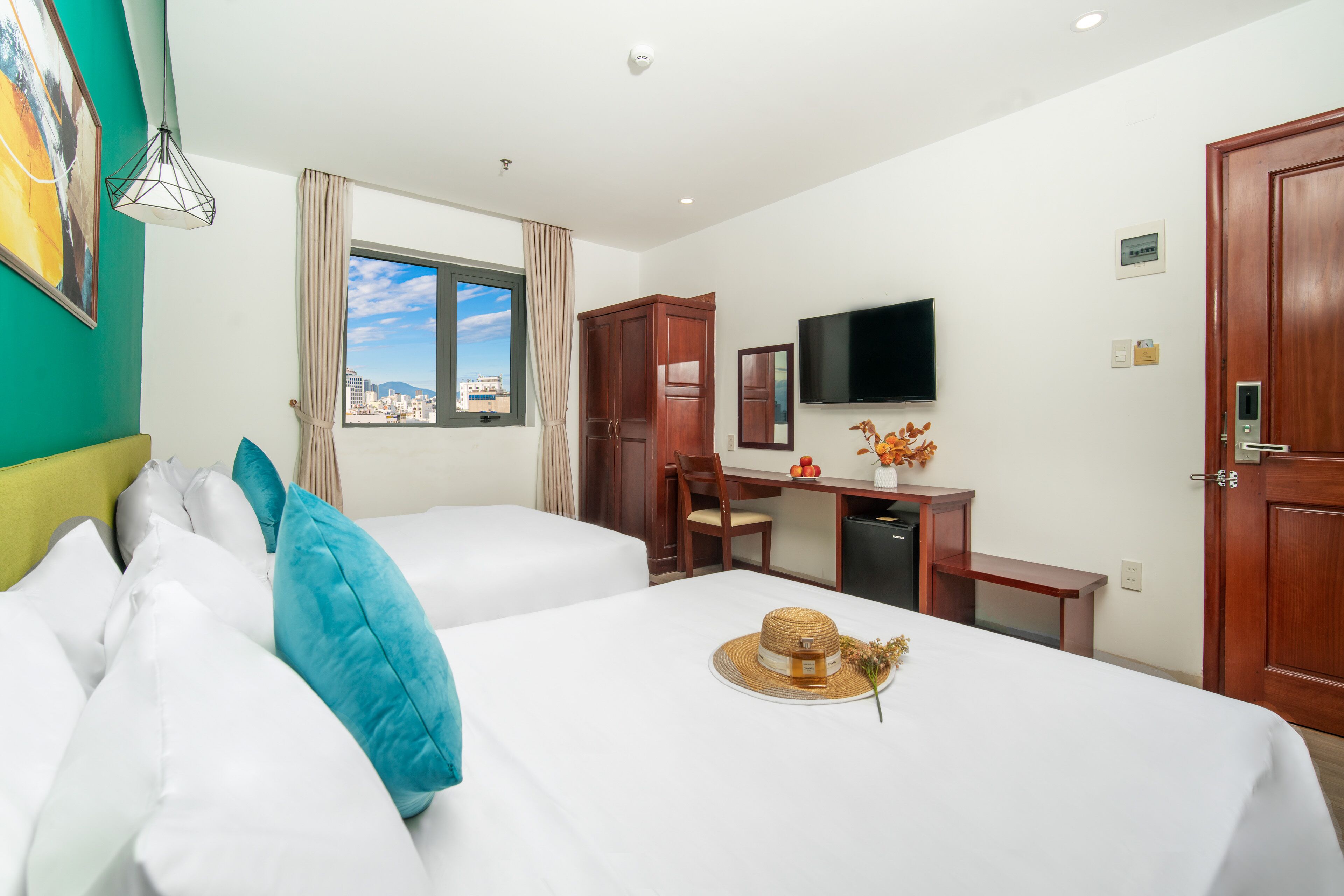 A hotel room with two beds, a desk, a television, and a view of the city.