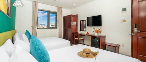 A hotel room with two beds, a desk, a television, and a view of the city.