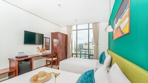 A hotel room with two beds, a desk with a chair, a TV, and a view of the city through large windows. - May Beach Hotel (Da Nang)