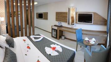 A hotel room with a bed, a desk, a chair, and a small table with cups and a teapot.