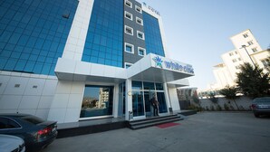 Un hotel moderno con un llamativo letrero 'White Star', entrada de vidrio y un estacionamiento con coches.