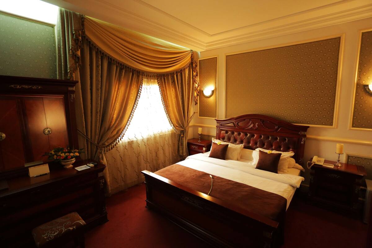 Ein traditionell eingerichtetes Hotelzimmer mit einem großen Bett, einem hölzernen Schminktisch, einem Schreibtisch und einem Nachttisch.