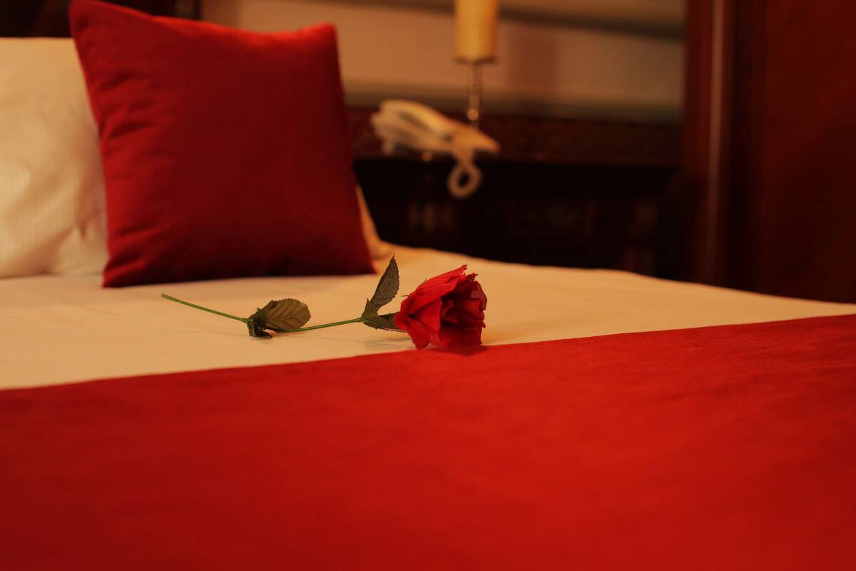 Ein Bett mit einer roten Rose und einem roten Kissen.