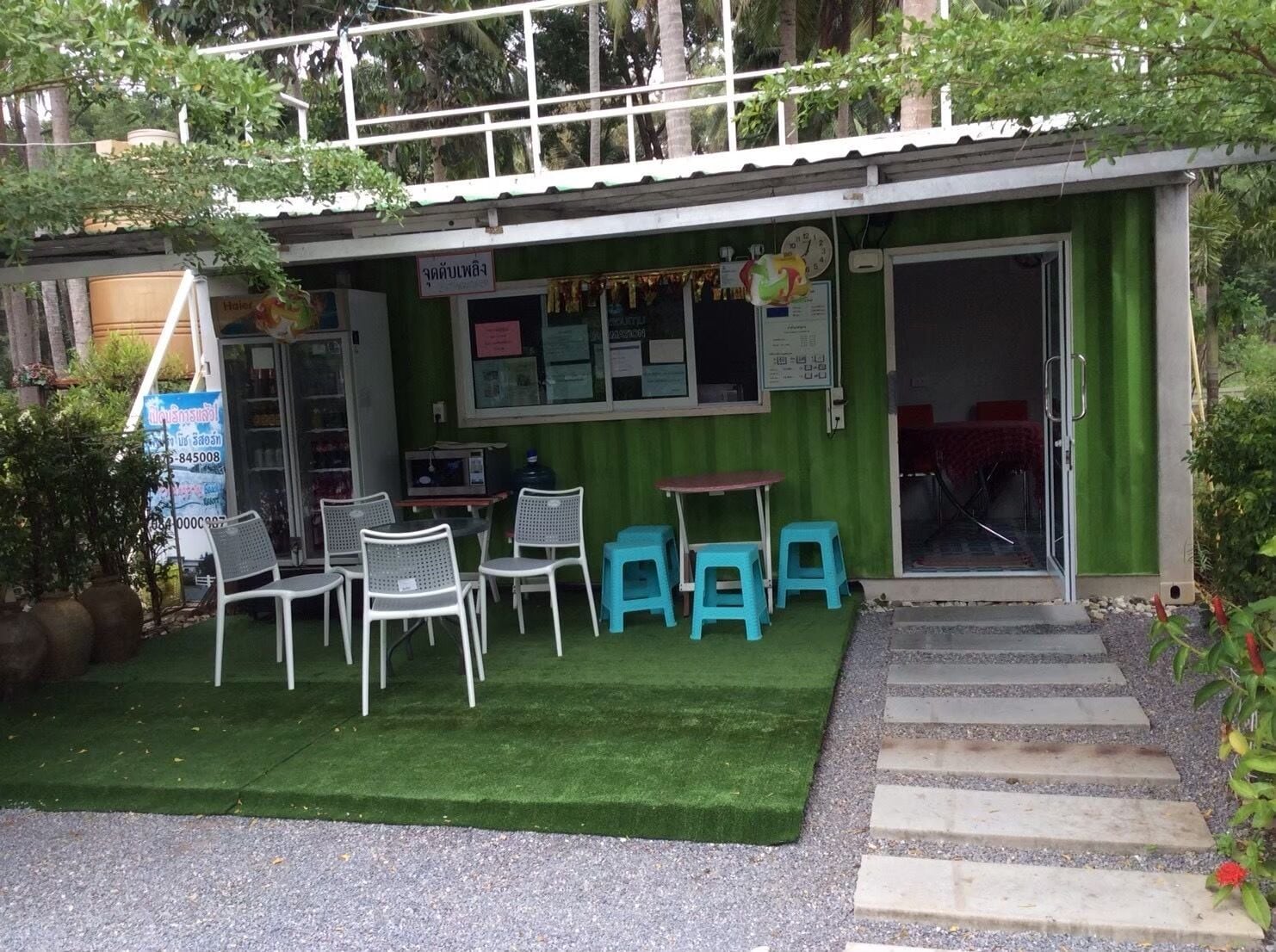 A small building with a green exterior, a glass door entrance, and a small outdoor seating area with chairs and tables.