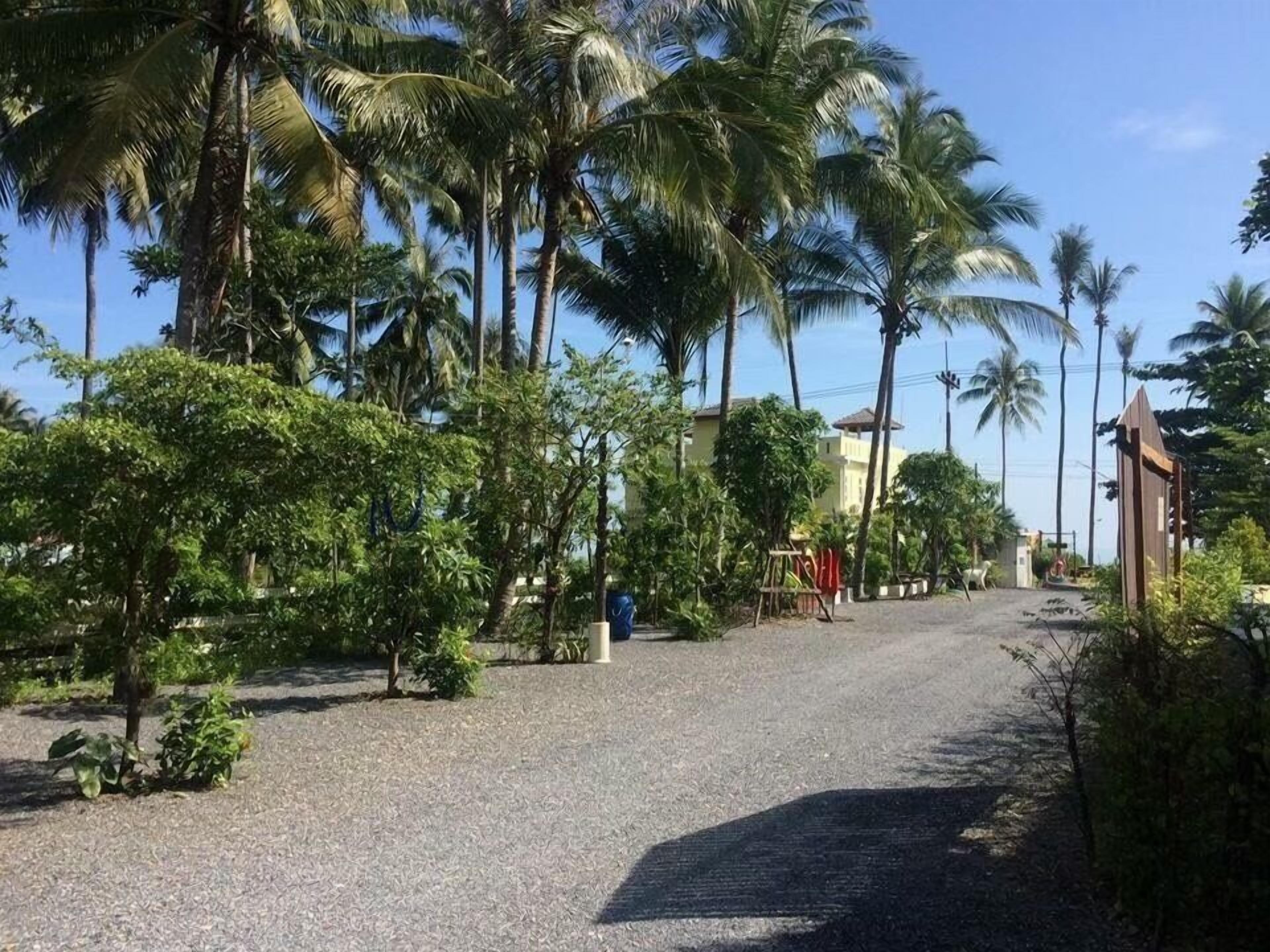 Un chemin pavé bordé de palmiers et de verdure, qui mène à un bâtiment doté d’un toit rouge.