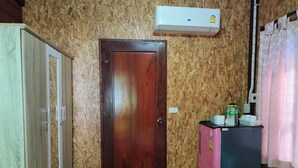 A room with a wooden door, a small pink refrigerator, and an air conditioning unit on the wall.