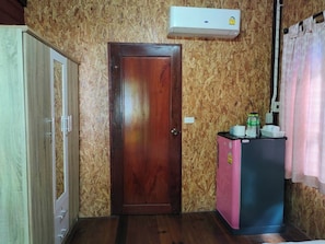 A room with a wooden door, a small pink refrigerator, and an air conditioning unit on the wall. - Phangpring Beach Resort (Tha Sala)
