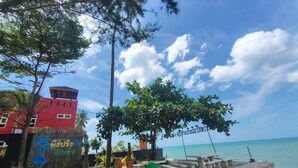 A beachside view with a red building, palm trees, and a clear sky.