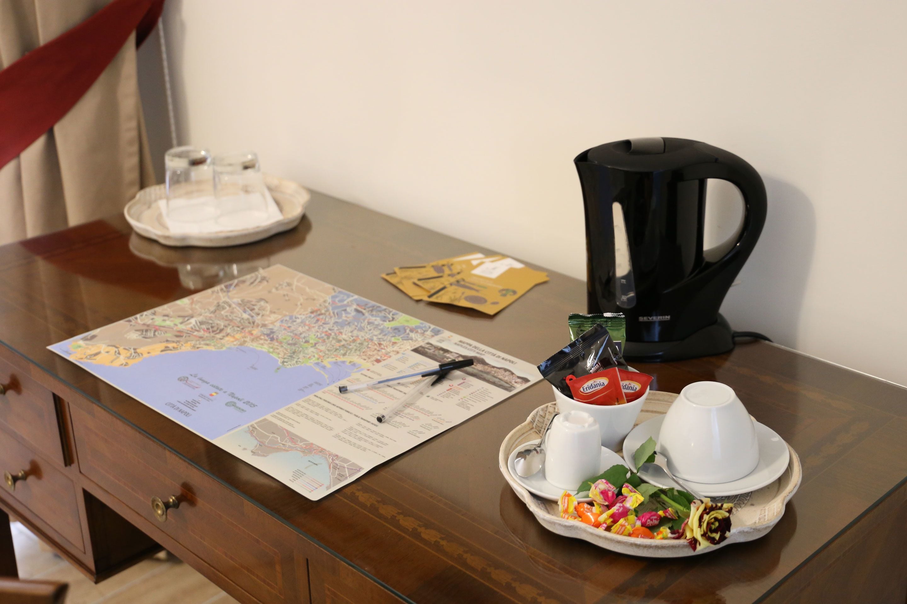 Un escritorio de madera con un mapa, una cafetera, una bandeja con aperitivos y una taza.