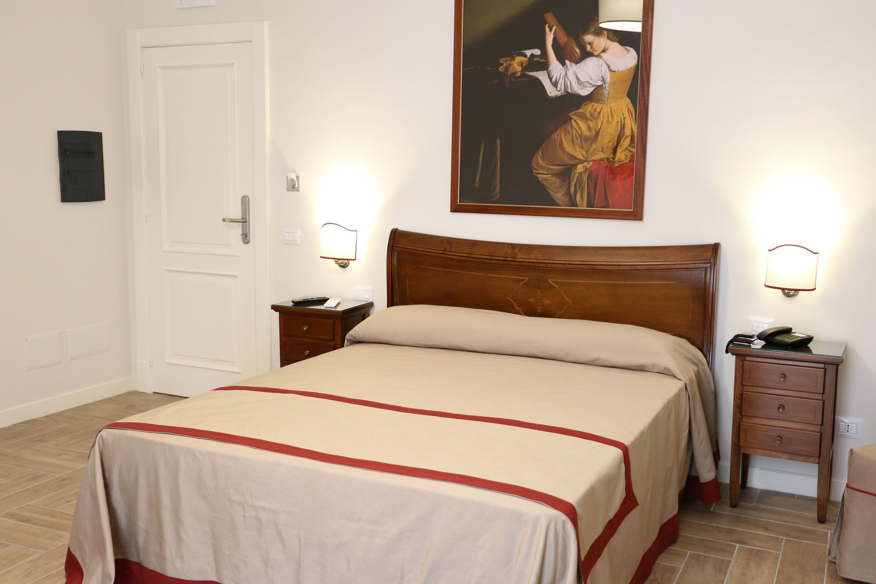 Une chambre d’hôtel avec un lit, des tables de chevet, une commode, un tableau au mur et une porte.