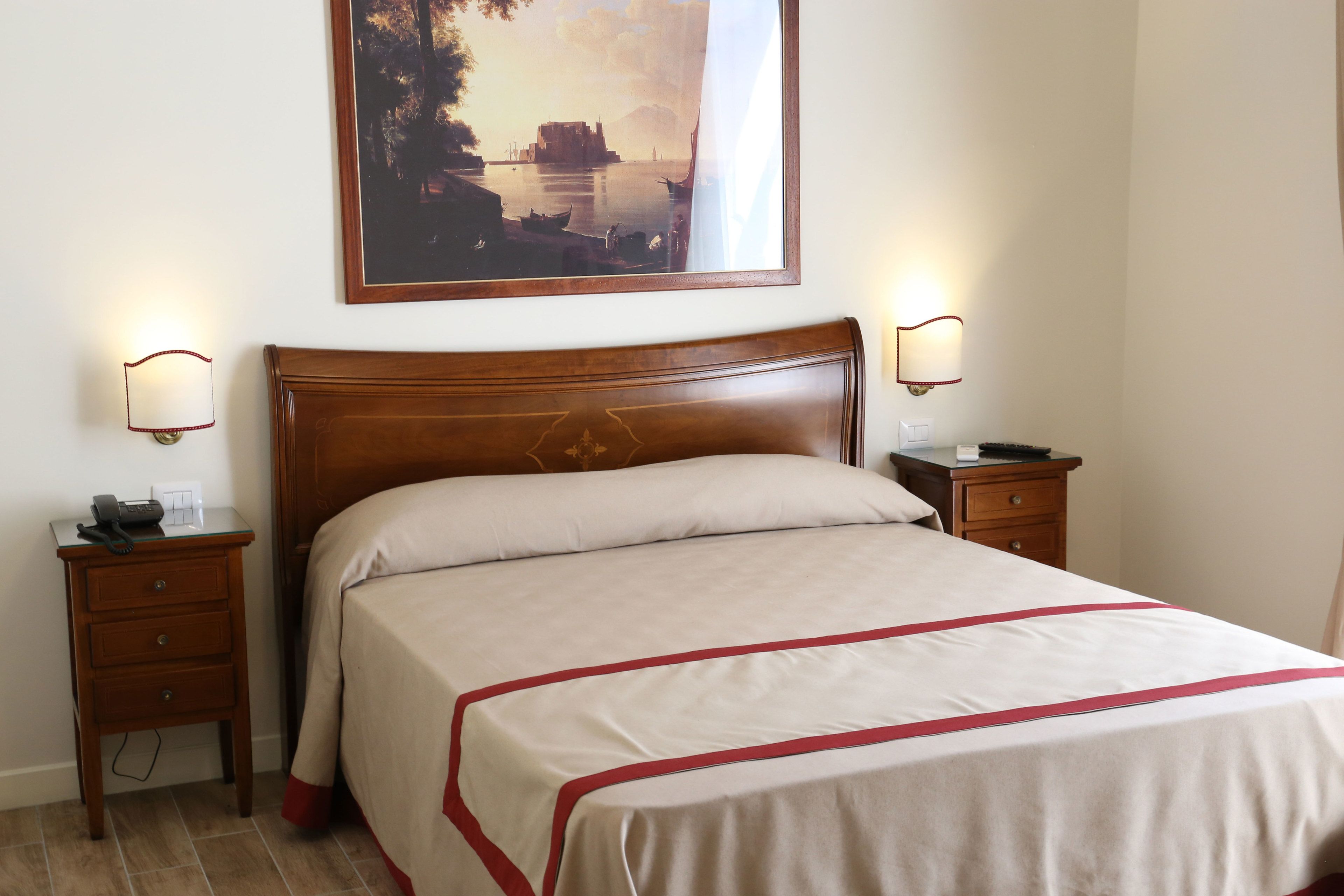 A neatly made bed with a wooden headboard, two bedside tables with lamps, a painting on the wall, and a telephone on one of the tables.