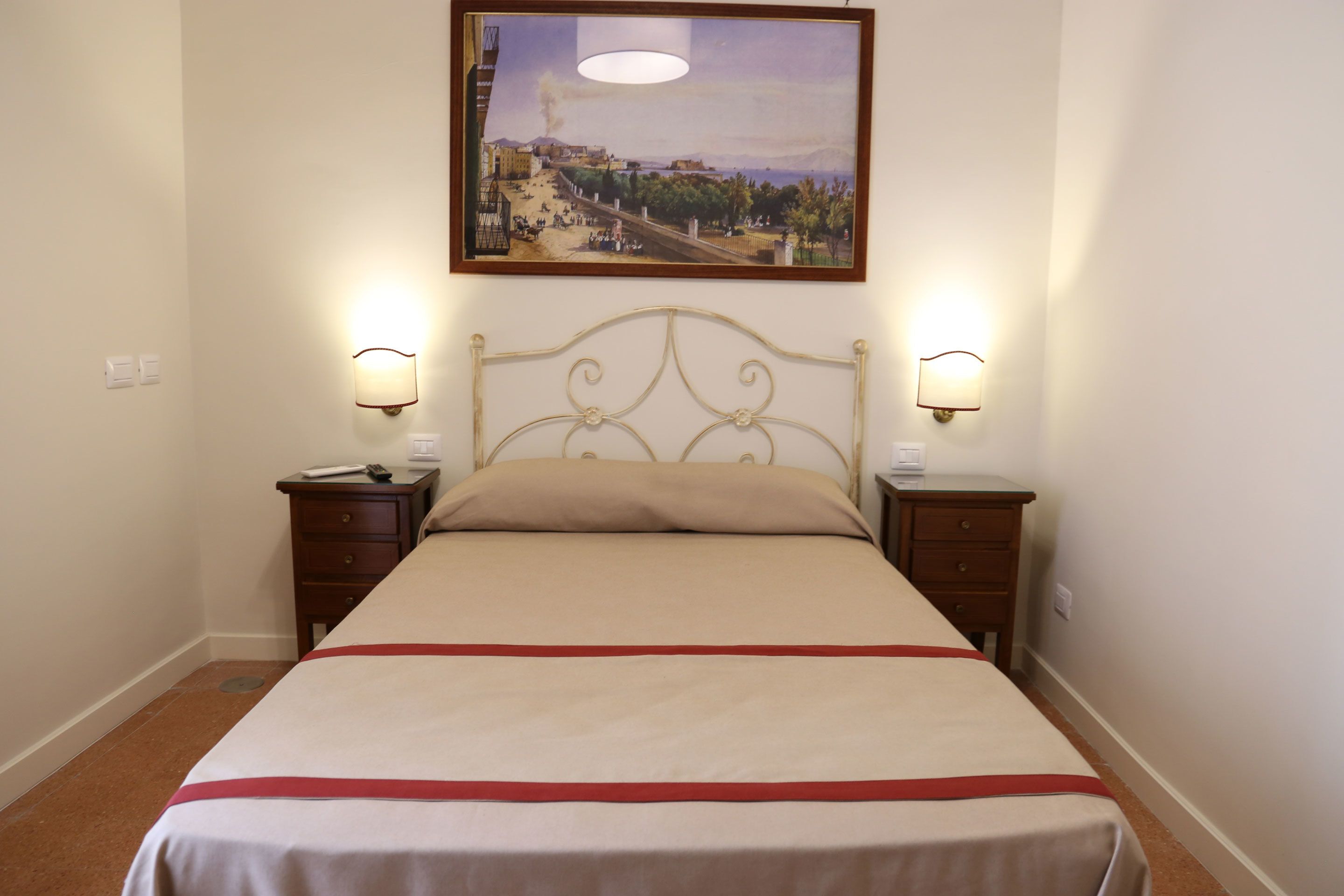Un letto rifatto con un tocco di colore rosso, due comodini con lampade e un quadro incorniciato sopra il letto.