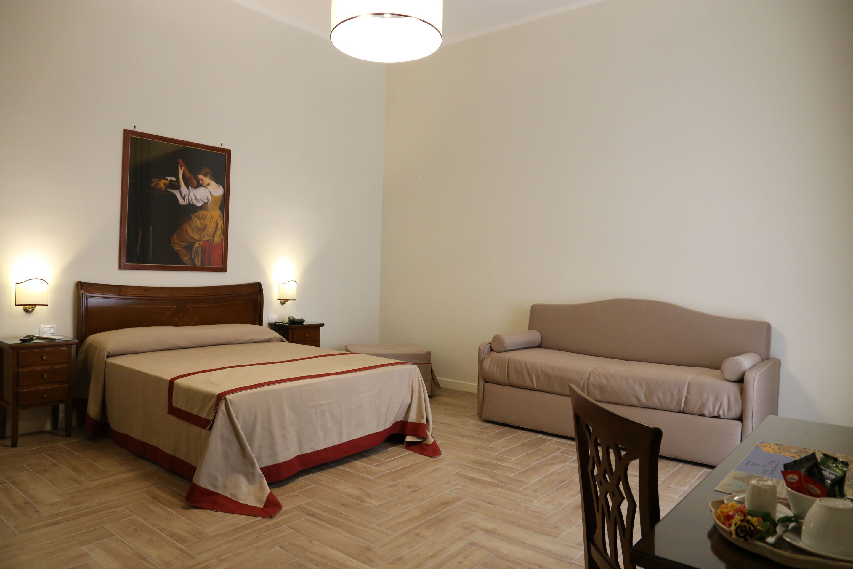 A hotel room with a bed, a sofa, a dining table, and a painting on the wall.