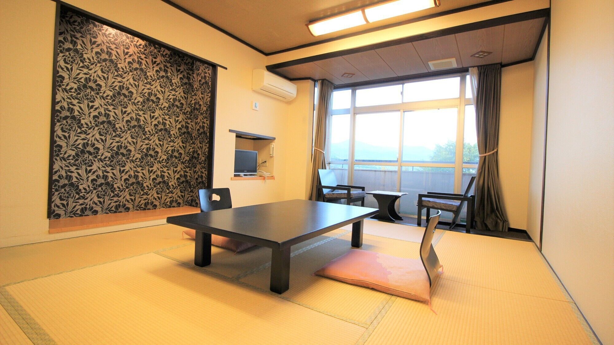Habitació amb sòl de tatami, una taula baixa, cadires, televisió i una finestra gran amb cortines.