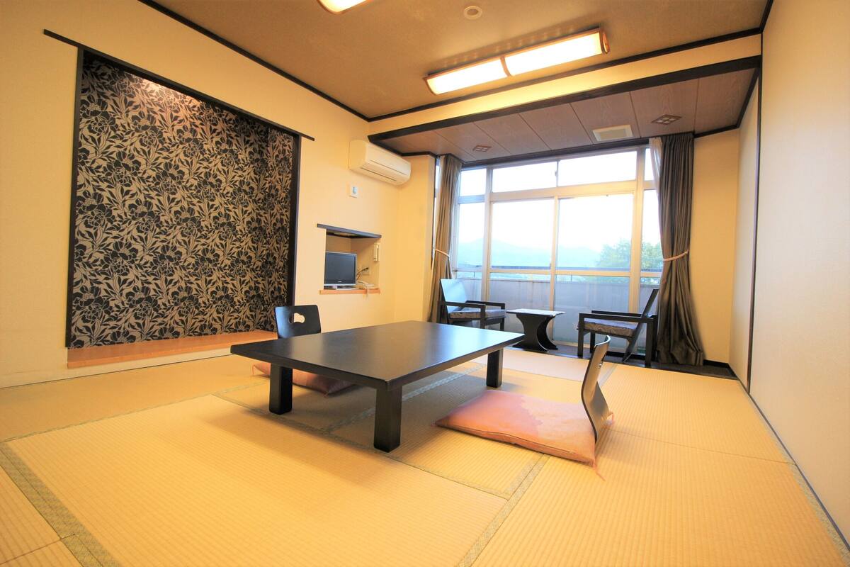 A tatami mat room with a low table, chairs, and a view through a large window.