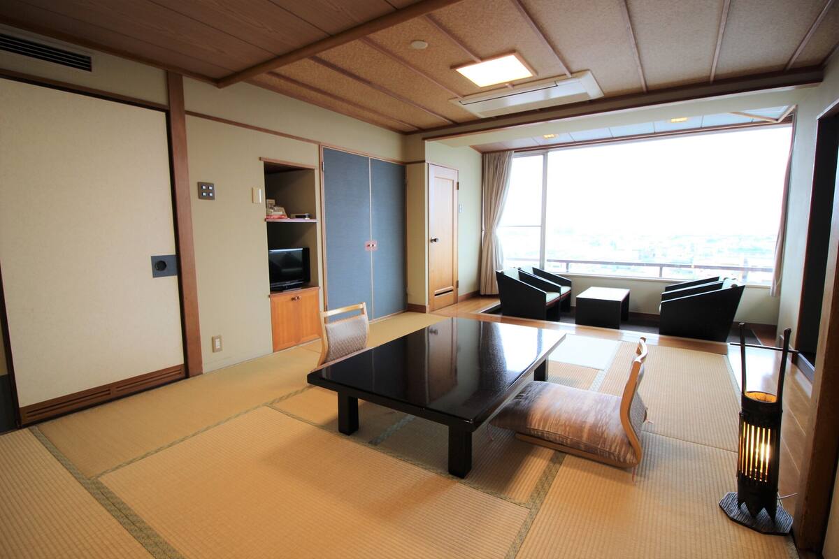 A traditional Japanese room with tatami flooring, a low table, cushions, and a sliding door.