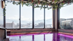 A room with large windows, a reflective floor, and a view of city buildings and mountains. - Hotel Hatta (Fuefuki)