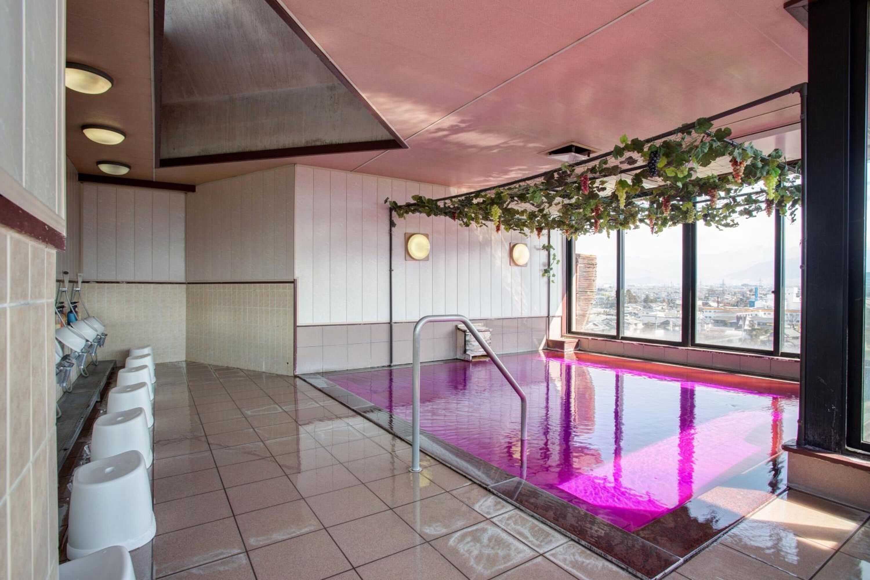 Una piscina interior moderna con paredes de vidrio transparente, suelo de baldosas y una fila de urinarios blancos a un lado.