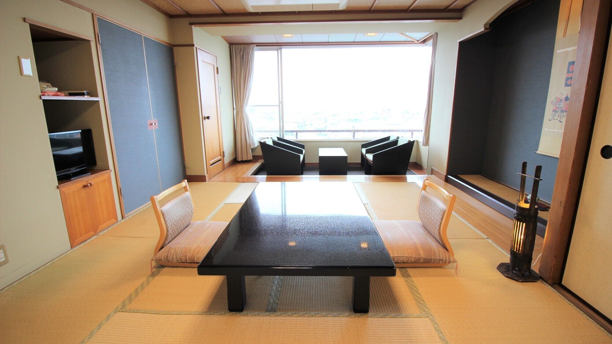 Habitació amb esteigs de tatami, una taula baixa, seients amb coixins, televisió i una finestra gran.