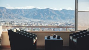 A room with a view of mountains and a cityscape. There are two chairs and a small table with teapots on it. - Hotel Hatta (Fuefuki)