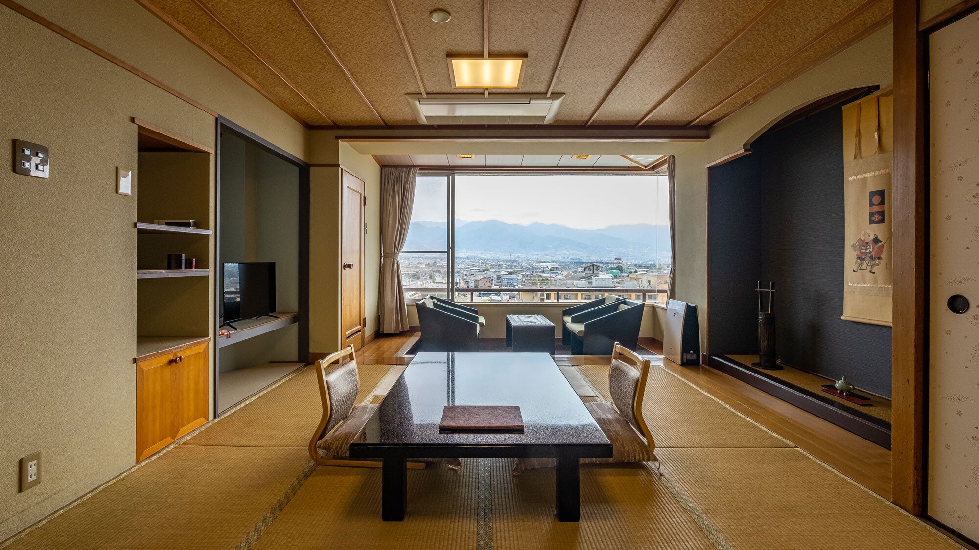 Habitació japonesa tradicional amb sòcols de tatami, una taula baixa i vista a un paisatge urbà a través de grans finestres.