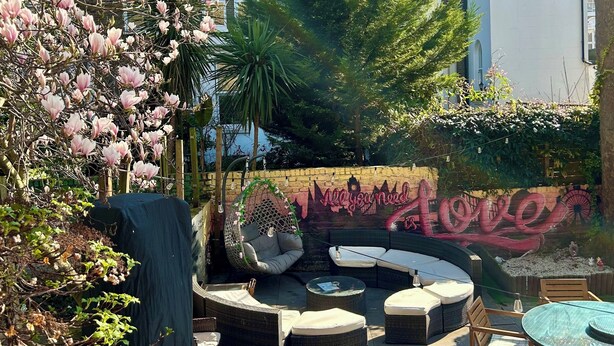 A patio area with outdoor seating, a hanging chair, and a mural with the text "All you need is love". - Saint James Backpackers (London)