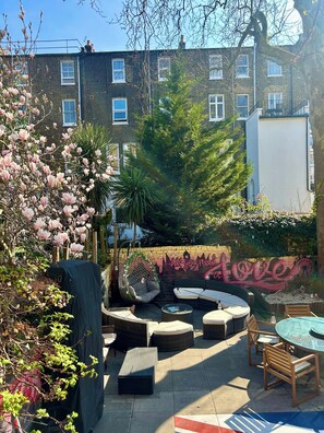 Un patio con mobiliario exterior, una silla colgante y un mural con el texto "All you need is love".