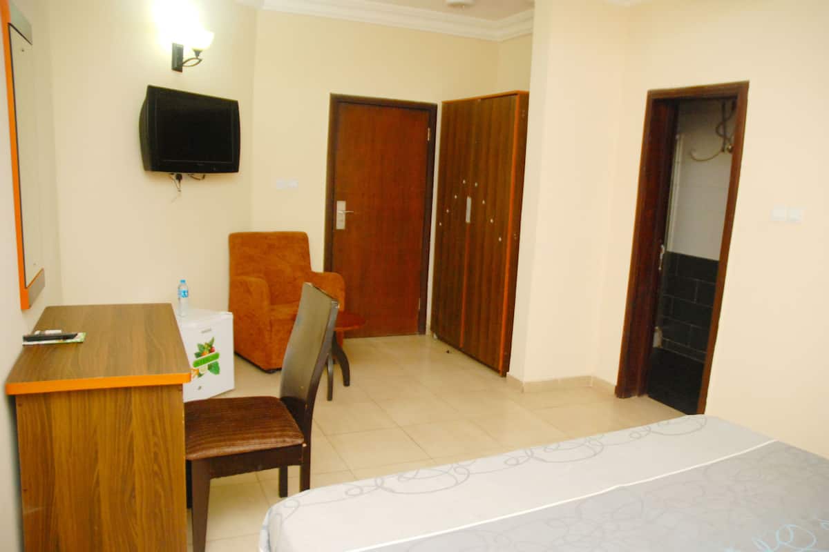A hotel room with a bed, a desk, a chair, a television, and a wardrobe.