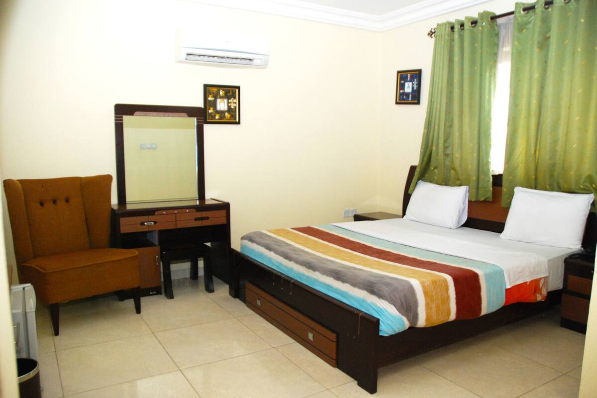 A bedroom with a bed, a desk, a chair, and a mirror.
