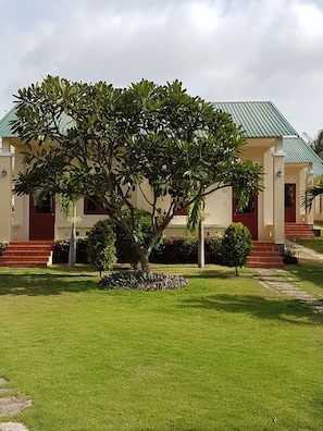 A building with a green roof, a well-maintained lawn, and a large tree in the center. - Herbal Hotel & Spa (Mui Ne)